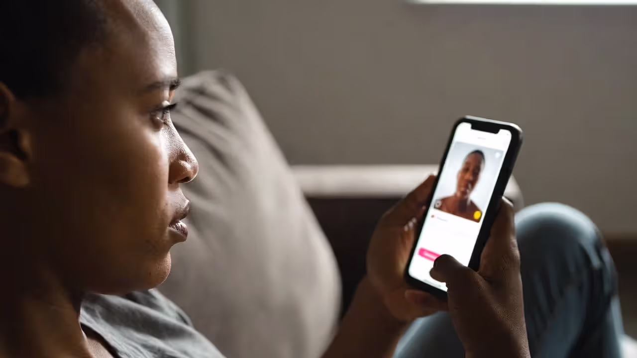 Person looking thoughtfully at dating app on smartphone while sitting alone